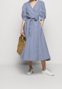 Blå och vit rutig klänning med puffärmar, knytmidja och utsvängd kjol, tillsammans med en beige väska och vita sneakers.