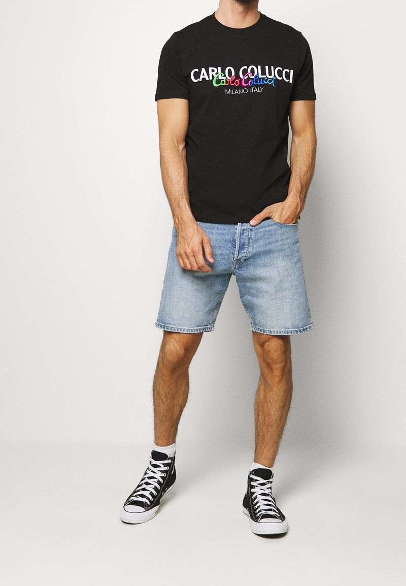 Camiseta de algodón negra con texto colorido, acompañada de pantalones cortos de mezclilla azul claro y zapatillas altas negras. Diseño sencillo y ajuste casual.