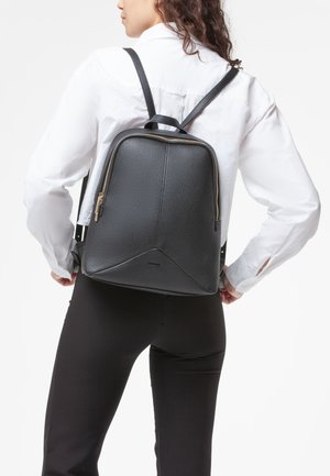 Zaino in pelle nera con finitura testurizzata, chiusura con zip e pannello inferiore triangolare. Presenta spallacci regolabili e dettagli in metallo dorato.