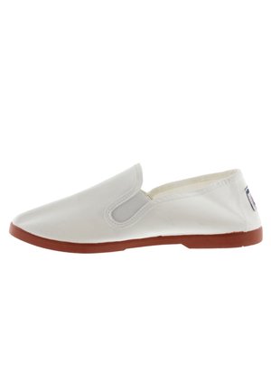 Zapato tipo slip-on de lona blanca con acentos elásticos en los laterales y suela de goma marrón. Textura suave, diseño minimalista y forma de punta redondeada.