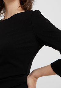 Abito nero aderente con maniche a tre quarti, scollatura rotonda, tessuto liscio e dettagli sottili nelle cuciture laterali.