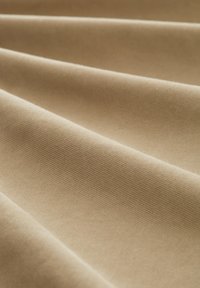 Beżowa bawełniana tkanina ułożona w fałdy, charakteryzująca się gładką fakturą i subtelnym diagonalnym wzorem splotu, prezentująca równomierne zabarwienie i miękkość.