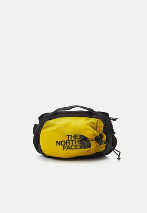 Kompaktowa czarno-żółta saszetka North Face z przednią kieszenią zapinaną na sznurek oraz górnym uchwytem na białym tle.