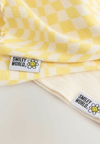 Geel en wit geblokt katoen met ribbeltextuur, met Smiley World labels met een glimlachende bloemenontwerp.