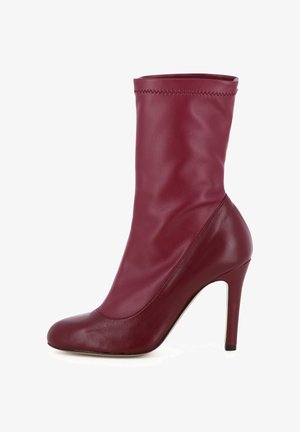 Stivale alto bordeaux con tacco, con una parte superiore in pelle liscia e aderente, punta arrotondata e design senza cuciture. Presenta una silhouette slanciata e affusolata.