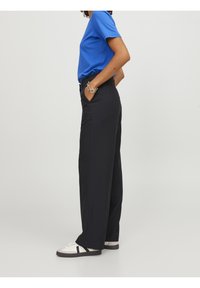 Blå kortärmad t-shirt kombinerad med högmidjade svarta byxor; byxorna har fickor och är gjorda av ett smidigt, lätt tyg.