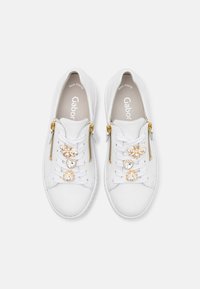 Weiße Ledersneaker mit goldenen Hardware-Elementen, dekorativen Verzierungen an den Schnürsenkeln und Reißverschlussakzenten. Texturierte Gummisohle für besseren Halt.