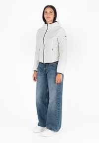 Witte, lichtgewicht jas met een capuchon, rits aan de voorkant en twee zijzakken. Gecombineerd met wijde blauwe jeans en witte sneakers.