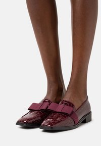 Chaussures plates bordeaux à texture crocodile, avec un large nœud en tissu sur l'avant et un petit talon bloc pour la stabilité.