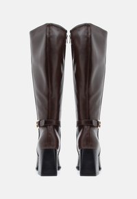 Hnědé kožené nadkolenní boty s hladkým povrchem, širokým podpatkem a bočním zipem, s páskem a detailním kovovým přezkou.