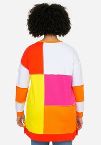 Oversized mikina v barevném bloku s oranžovými, růžovými, bílými, žlutými a červenými částmi. Měkká tkanina, dlouhé rukávy, boční rozparky a prošívané detaily.
