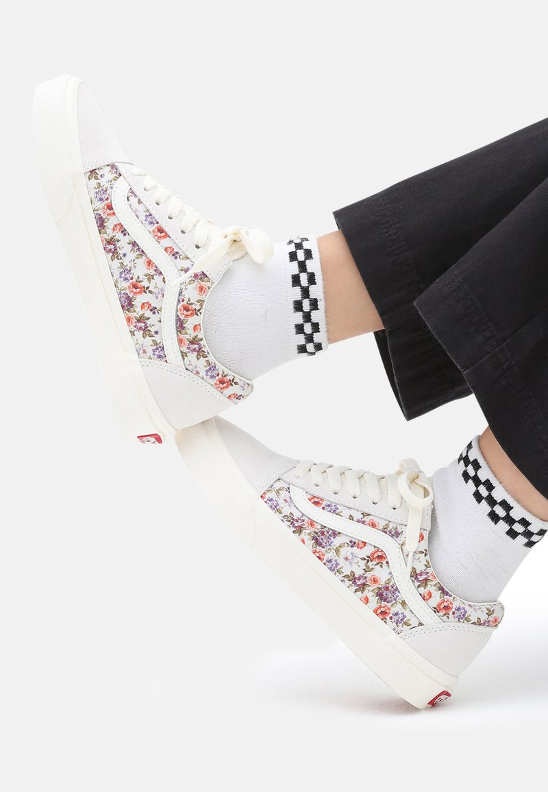 Sneakers bianchi con stampa floreale, caratterizzati da un design low-top, chiusura con lacci e suole testurizzate. Abbinati a calzini a quadretti.