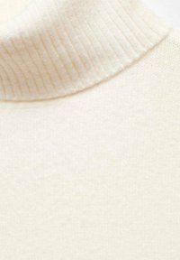 Detailní záběr na krémově bílý žebrovaný rolák, který ukazuje jemnou texturu pletené látky a detail překlopeného límce.