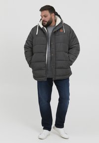 Grey puffer jacket with a hood, featuring a beige fleece lining, wooden button accents, and a casual fit. Worn over a grey sweater and blue jeans.