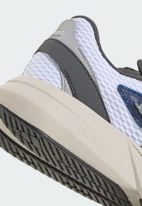 Sneaker with a textured white mesh upper, gray rubber accents, and a light beige sole featuring a patterned tread. "LIGHTSTRIKE" is embossed.
