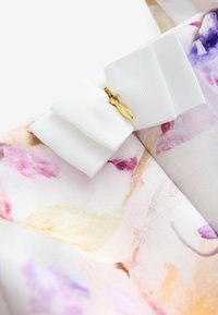 Robe avec un motif floral pastel comprenant des violets et des roses doux, complétée par un nœud texturé blanc avec un détail de fermoir en or.