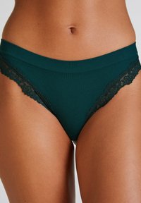 Tealfarbene Rippunterwäsche mit dekorativen schwarzen Spitzenakzenten an den Seiten und einem glatten Bund. Weicher Stoff, figurbetonter Schnitt.