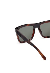 Lunettes de soleil écaille de tortue avec verres verts foncés, forme angulaire, monture en plastique texturé et logo "GUESS" sur la branche.