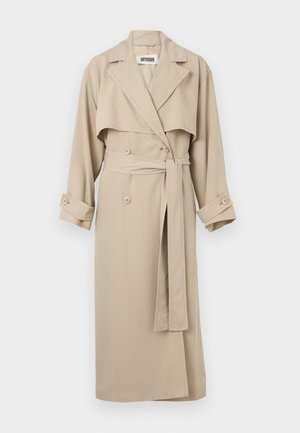 Trench coat beige lungo con ampi revers, bottoni doppiopetto, cintura in vita e polsini con bottoni, appeso su uno sfondo bianco.