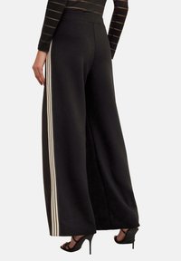 Svarta vida byxor i mjukt tyg, med krämfärgade sidostrimmor. Hög midja och skräddarsydd silhuett förbättrar komfort och rörelsefrihet.