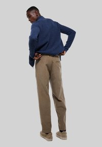 Pull bleu marine à côtes avec un col montant, associé à un pantalon en velours côtelé marron clair. Le modèle se tient avec les mains sur les hanches, portant des chaussures beiges.