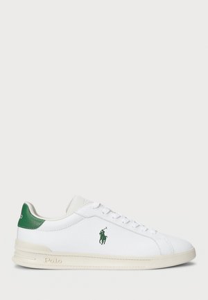 Witte lage sneaker met groene hielstuk, groen Polo-logo op de zijkant, witte veters en een beige zool.