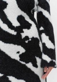 Mustat ja valkoiset kuviollinen neule, jossa on pehmeä ja pörröinen rakenne. Ominaispiirteenä on selkeä lehmän kuvio. Pitkät hihat, joissa on hiukan rispaantuneet resorit.