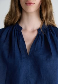 Blusa in lino navy con scollo a chiave, dettagli arricciati vicino al colletto e una vestibilità rilassata con una finitura testurizzata.