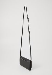 Geantă crossbody din piele neagră cu un finisaj texturat, partea superioară curbată, cusături albe și o curea ajustabilă. Formă compactă, rectangulară.