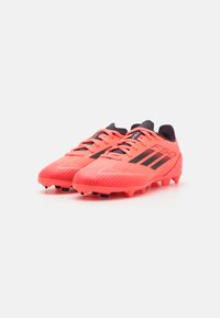 Botas de fútbol de color rosa brillante con acentos y cordones negros. Presentan una parte superior texturizada y tacos moldeados para una mejor tracción.