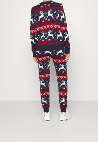 Mörkblå stickad jultröja och byxor med vita och röda renar, hjärtan och snöflingor. Ribbad ärm- och midjeband, kombinerat med vita sneakers.