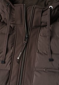 Close-up of a brown puffer jacket with a front zipper and two drawstrings hanging from the hood.