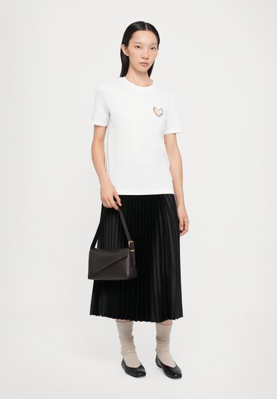 Hvit t-skjorte med hjerteformet broderi, plissert svart skjørt, beige sokker, svart håndveske og svarte leiligheter.