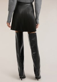 Svart veckad kjol i konstläder med hög midjeresår, kombinerad med glansiga svarta långa stövlar som går upp till låren, med spetsiga klackar och slät yta.