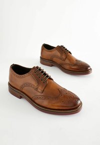Brune lædersko med brogue-detaljer, snørebånd-design og rund tå. Sålen har en kontrastfarvet farve.