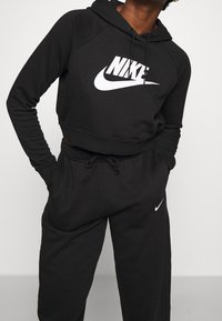 Black cropped hoodie with white Nike logo, paired with black joggers featuring a small Nike swoosh. Made of soft, textured material.
