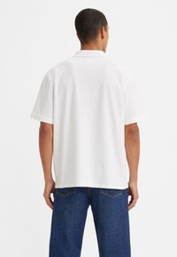Hvit kortermet polo-shirt med en uformell passform, med en klassisk krage og en jevn bomullstekstur. Enkelt design, ingen synlige mønstre.