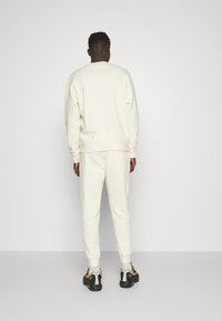 Cremefarvet sweatshirt og joggingbukser sæt, lavet af blødt stof, med ribstrikkede manchetter og talje, bæret med sorte og gule sneakers.