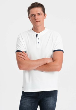 Witte polo met korte mouwen en een textuurafwerking, marineblauwe accenten op de kraag en mouwen, en een placket met twee knopen.