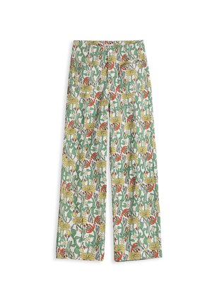 Mujer de pie, vistiendo una blusa beige de manga larga con bordado en las mangas y pantalones de talle alto y pierna ancha con estampado colorido de flores y pájaros.