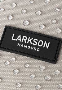 Tissu gris avec un motif de points argentés en relief et une étiquette noire rectangulaire affichant "LARKSON HAMBURG" en lettres blanches.
