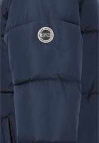 Marineblaue gepolsterte Jacke mit einem runden Logo-Patch, auf dem der Text "ZIGZAG" steht, und einem hervorgehobenen gesteppten Look sowie einem weichen Material.