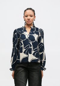 Bluza albastru navy cu model abstract de frunze crem, mâneci lungi și nasturi în față, confecționată dintr-un material texturat și cu manșete strânse.