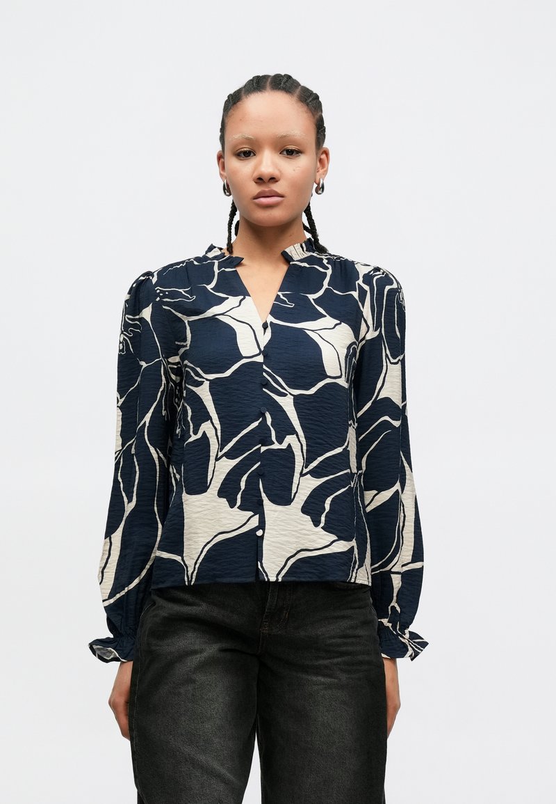 Bluza albastru navy cu model abstract de frunze crem, mâneci lungi și nasturi în față, confecționată dintr-un material texturat și cu manșete strânse.