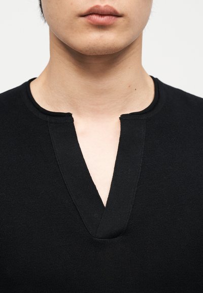 Κοντινό πλάνο του λαιμού και του κάτω μέρους του προσώπου ενός ατόμου που φοράει μαύρο πουκάμισο με υφή και γιακά V-κομμένο με εγκοπή.