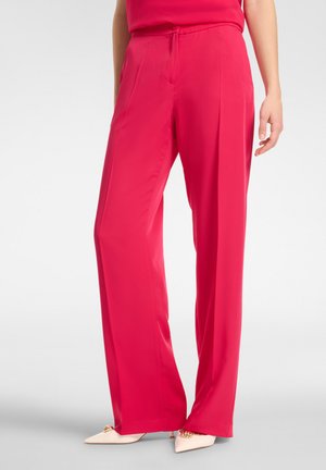 Pantalones de pierna ancha de un rosa intenso, hechos de una tela suave, con una cintura ajustable y bolsillos laterales sutiles. Combinados con zapatos de color claro.