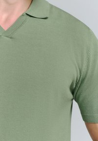 Korte mouwen polo shirt in lichtgroen, gemaakt van ribgebreide stof. Kenmerkt zich door een V-hals kraag en een aansluitend ontwerp met gestructureerde details.