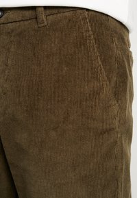 Pantalons en velours côtelé marron avec des côtes verticales, dotés de deux poches latérales, d'une fermeture à bouton et d'une finition en tissu texturé.