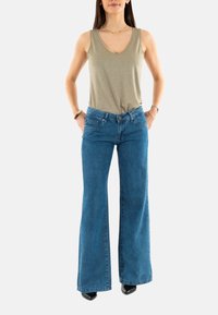 Top sin mangas de color gris claro con escote en V, combinado con unos vaqueros de talle alto y pierna ancha de color azul y unos zapatos de tacón negros. Diseño simple, sin patrones.