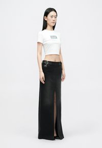Fekete farmer szoknya elöl hasítékkal, övhurkokkal és két fém részlettel. Egy illeszkedő fehér crop top-pal párosítva. Egyszerű és modern dizájn.